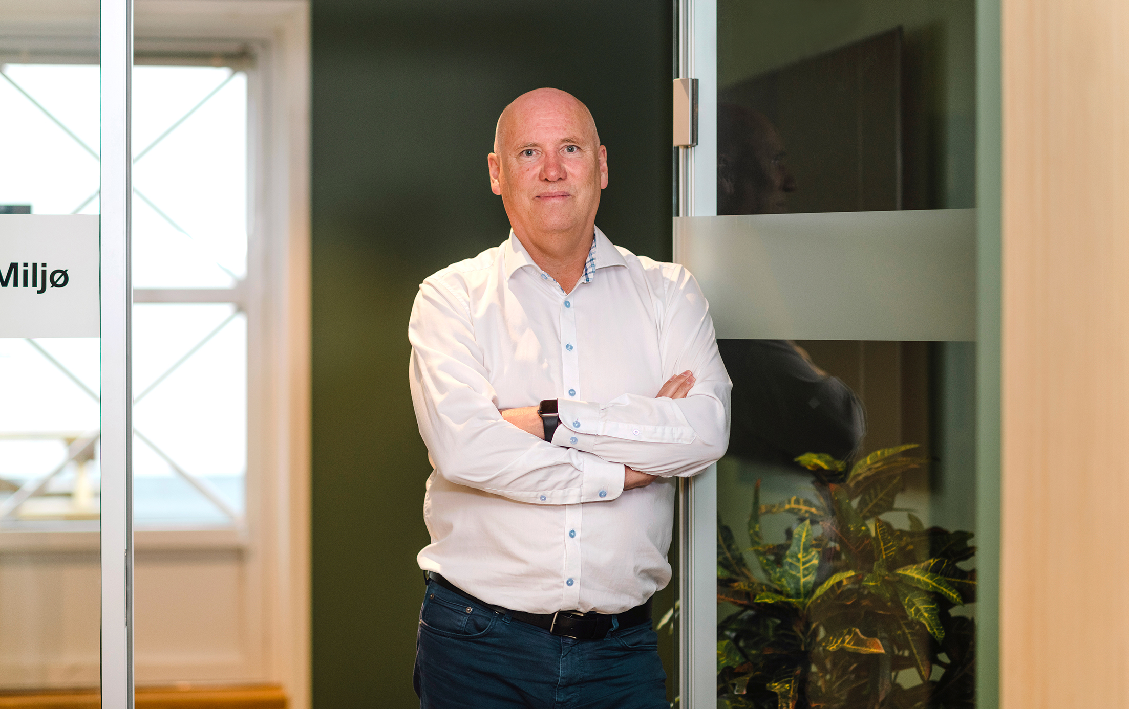 Portrett av ansatt Øivind Holm som står lent opp mot en dørkarm på en glassvegg 